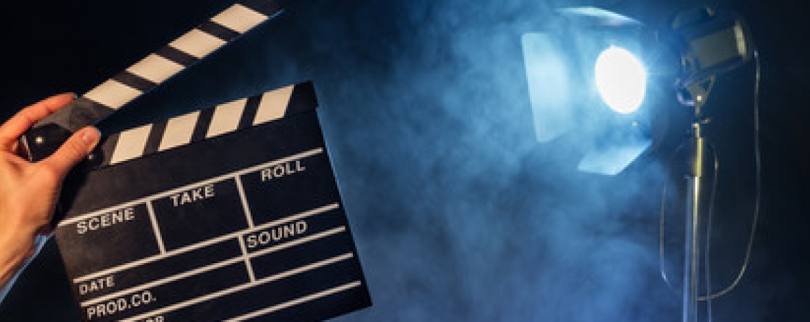 une main qui tient un clap de cinéma avec un projecteur en arrière plan